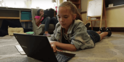 A young girl laying on the ground while working on a laptop.