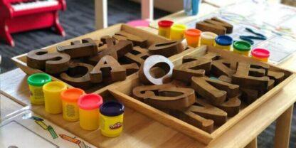 A pile of wooden alphabet letters stacked on table next to Play-Doh.