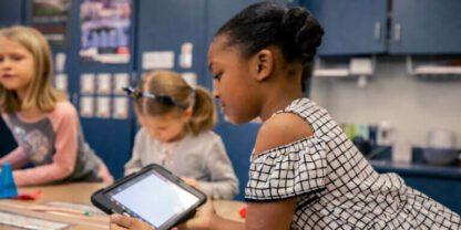 Students working together on tablets at a large round table.