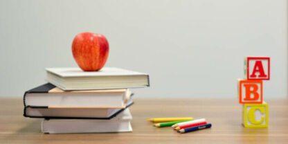 An apple sitting on top of a stack of books next to some alphabet blocks.