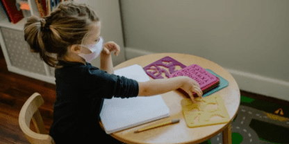 A girl wearing a mask and working on activities at a small round table.