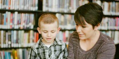 A teacher reading to a student in a library.