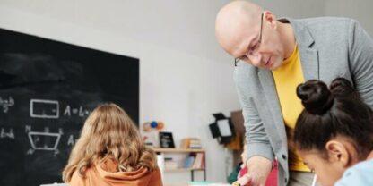 A teacher leaning over a table to provide assistance to a student.