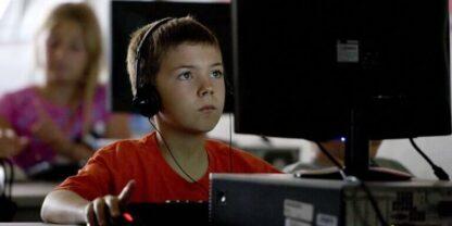 A young boy with headphones on looking at a computer screen.