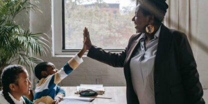 A teacher giving a high five to her student across the table.