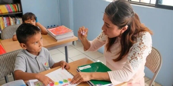 A teacher or principal sitting at a desk with a student and explaining something.