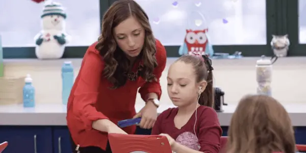 A teacher leaning over a student's shoulder to point something out on an iPad.